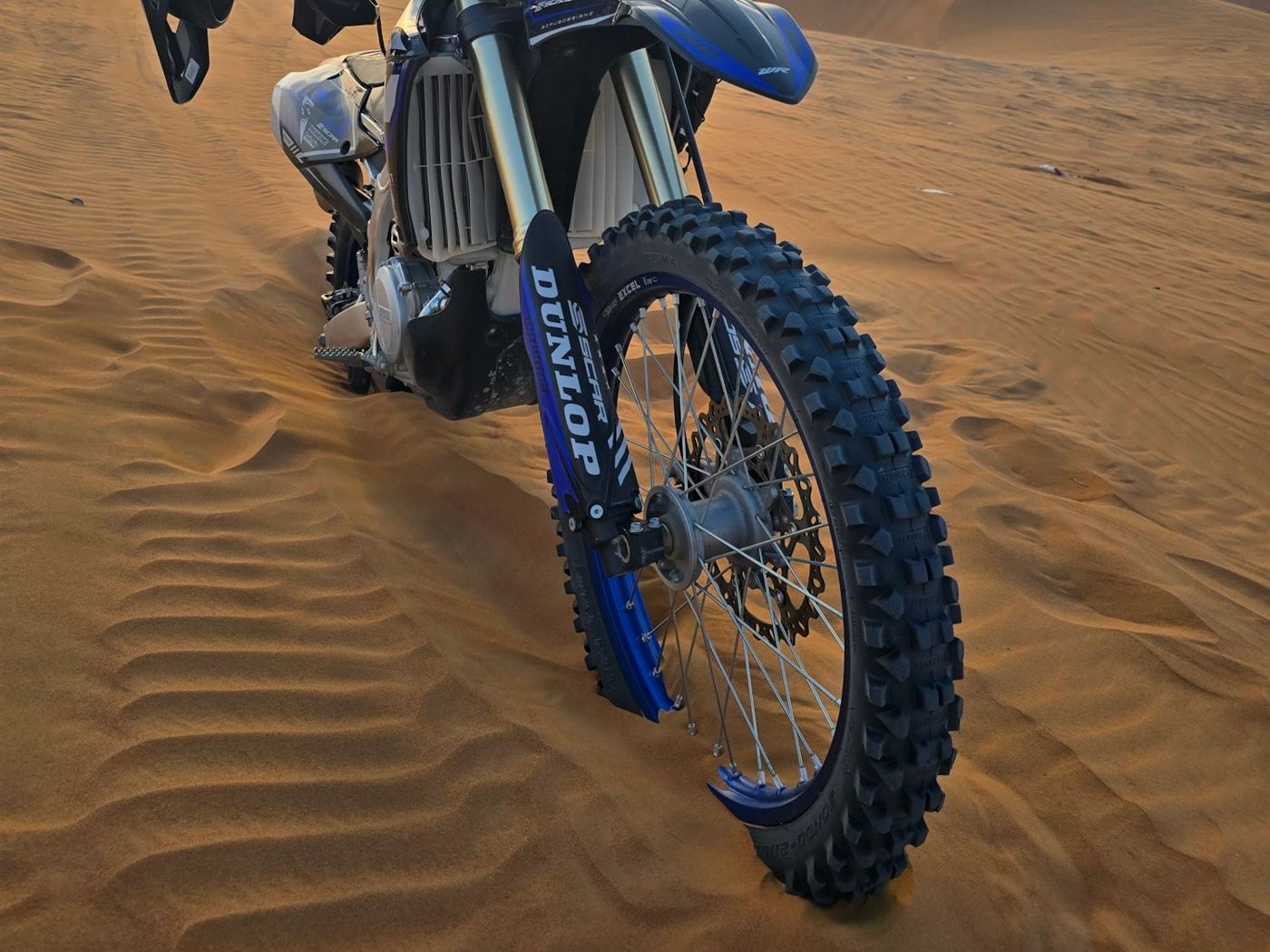 Close-up of the front knobby tyre and fork of a Yamaha dirt bike on desert sand