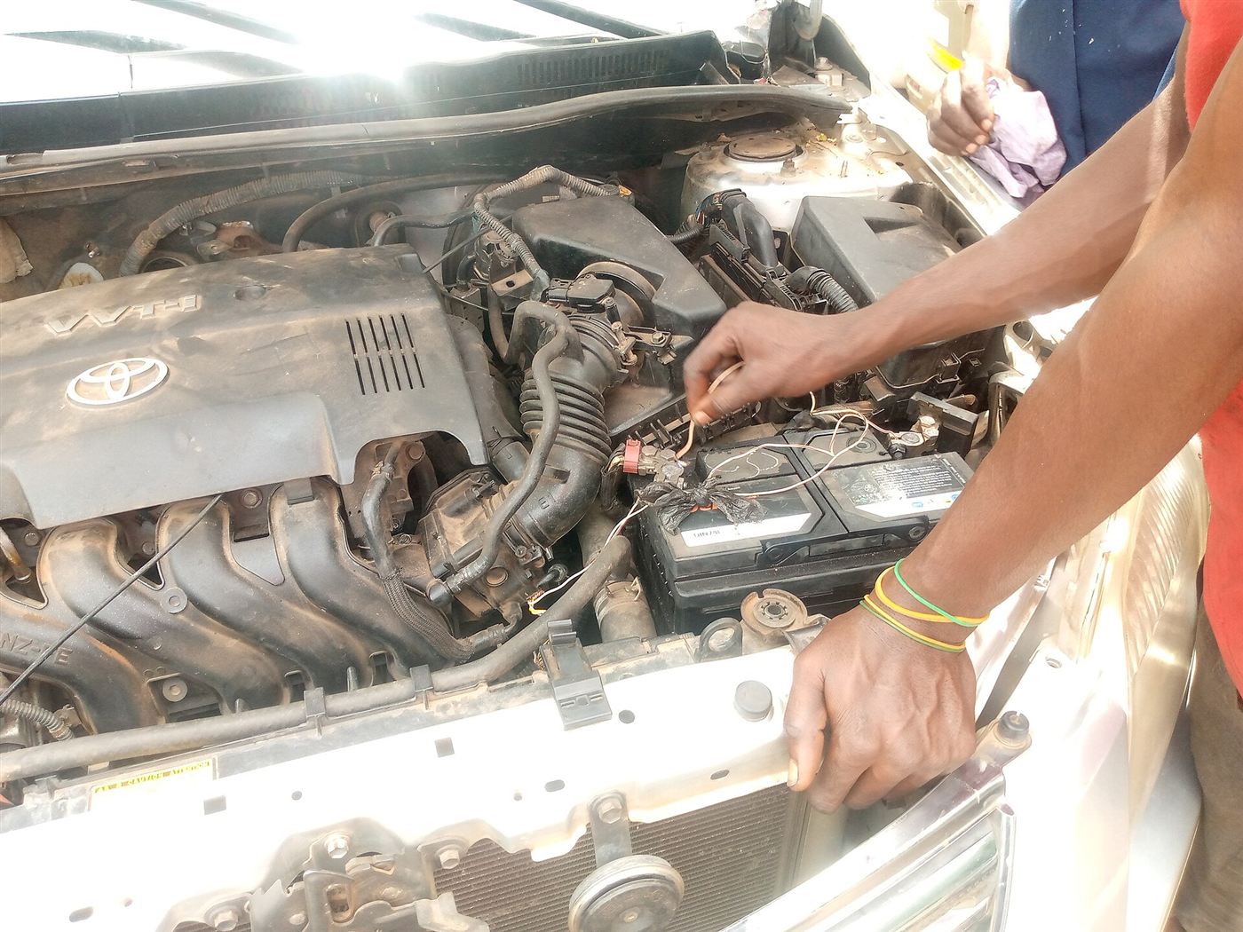 Mechanic's hands working at the battery in a car engine bay