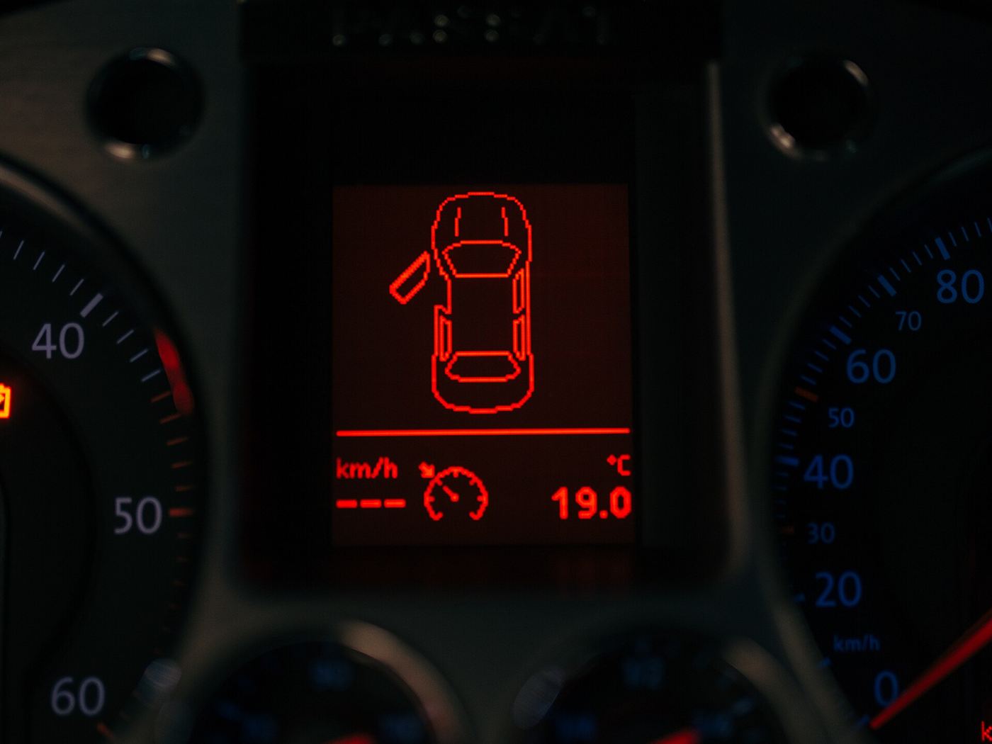 Car instrument cluster at night with a red warning light showing on the display
