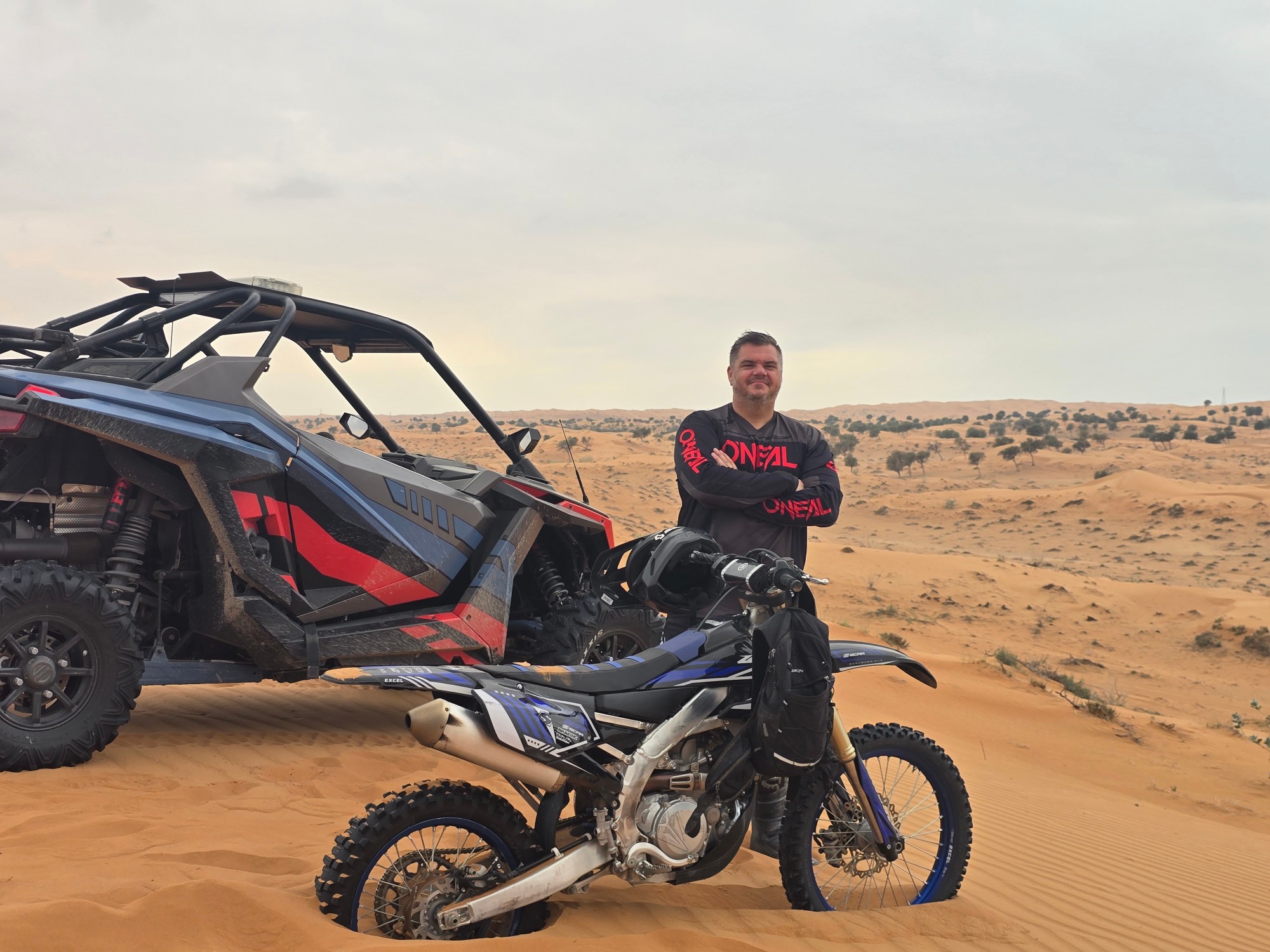 Rider standing beside a Yamaha dirt bike and a Polaris RZR in the Ras Al Khaimah desert
